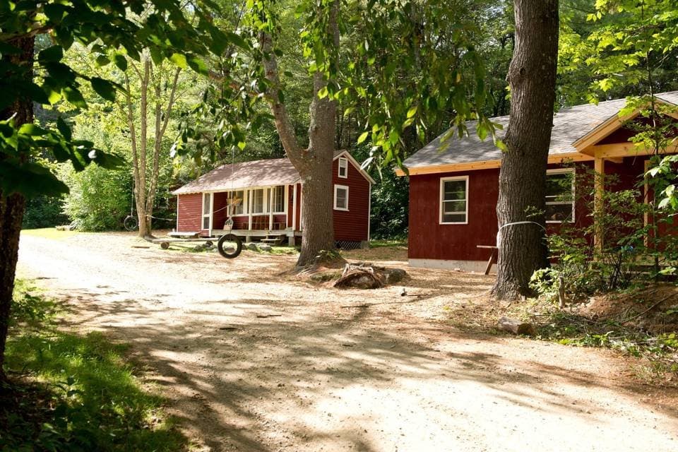 Two red cabins among the trees at Windsor Mountain, with a tyre swing outside.